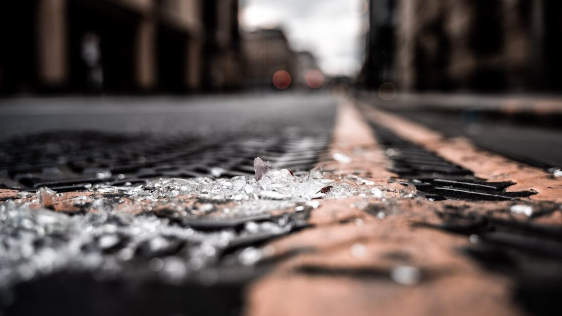Close-up of broken glass pieces scattered on a city street with blurred buildings.